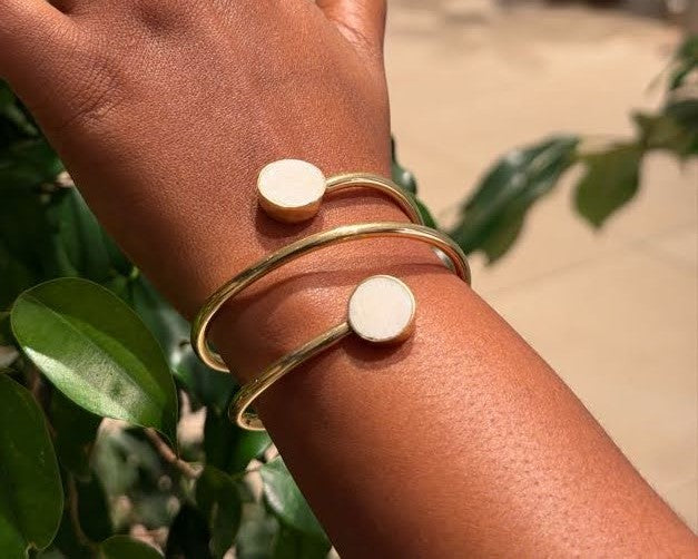 Chania Bangle – handcrafted brass open cuff with disc ends worn on wrist against green foliage