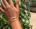 Ewaso Bangle – handcrafted brass stacking bangles worn on wrist against green foliage