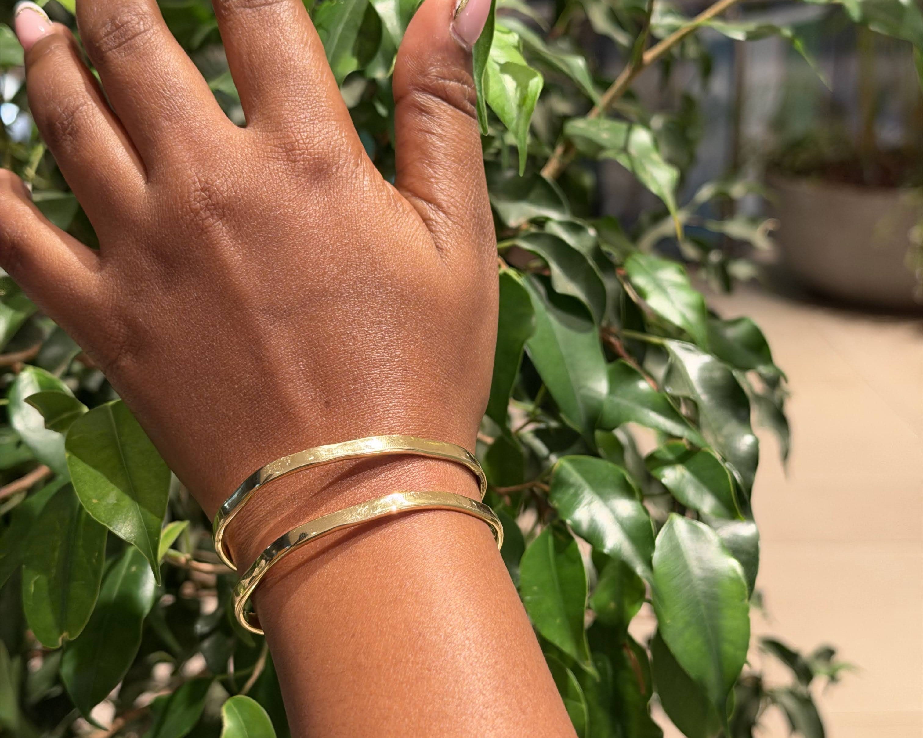 Ewaso Bangle – handcrafted brass stacking bangles worn on wrist against green foliage
