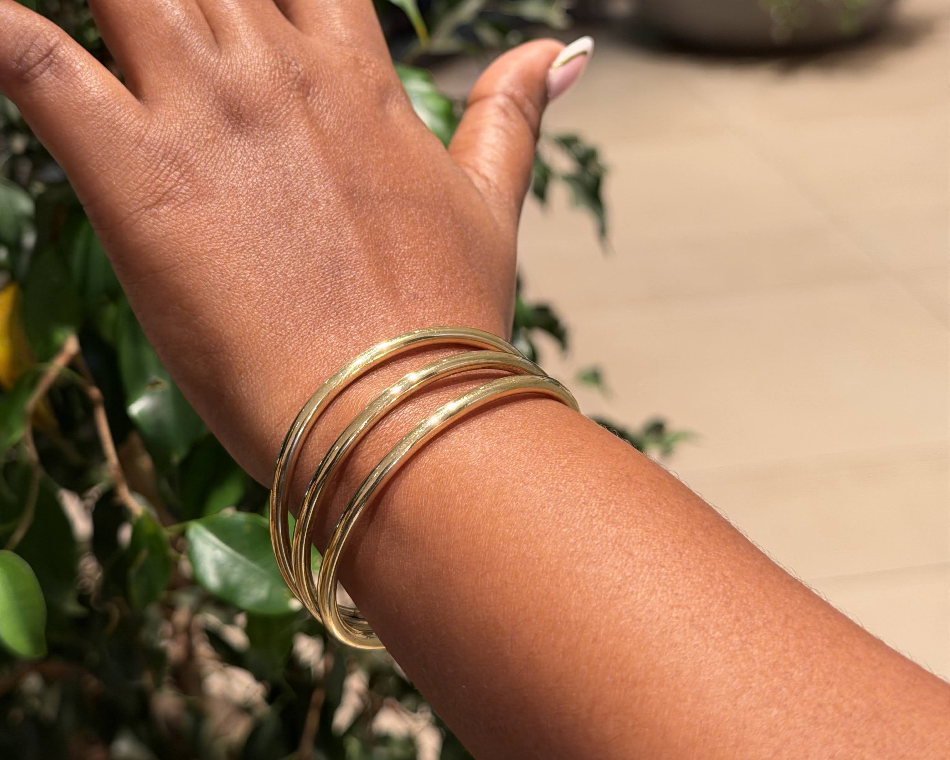 Ololua Bangle – handcrafted brass stacking bangles worn on wrist, layered look against green foliage