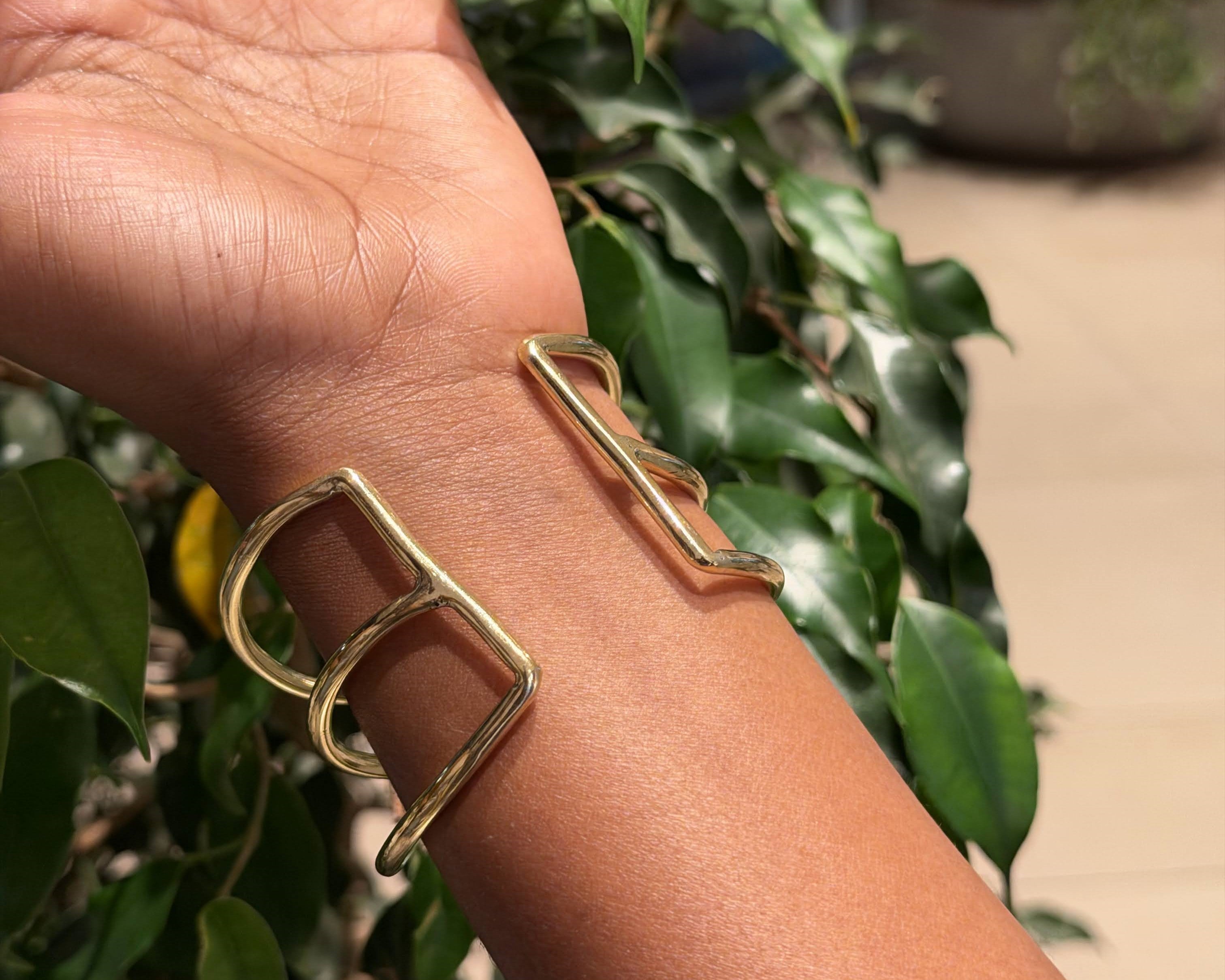 Suswa Bangle – handcrafted brass geometric double-frame cuff worn on wrist against green foliage