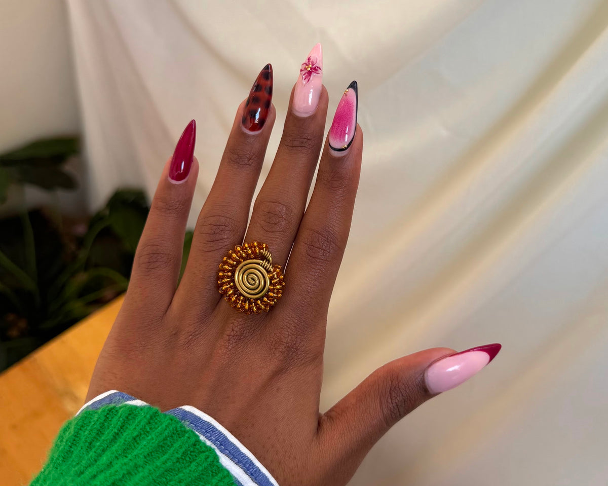 Nuru Ring Brown - circular beaded ring with spiral gold centre and amber-brown seed beads worn on hand